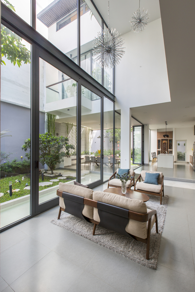 Phòng khách nối liền với khu vực phòng ăn, nhà bếp theo hình chữ L. Nếu tường kính xóa đi ranh giới trong - ngoài thì thông tầng đã xóa nhòa ranh giới giữa bên trên và dưới, giúp phòng khách thông thoáng với không gian mở rộng cả ba chiều.